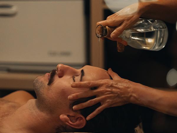 man getting oil poured over forehead